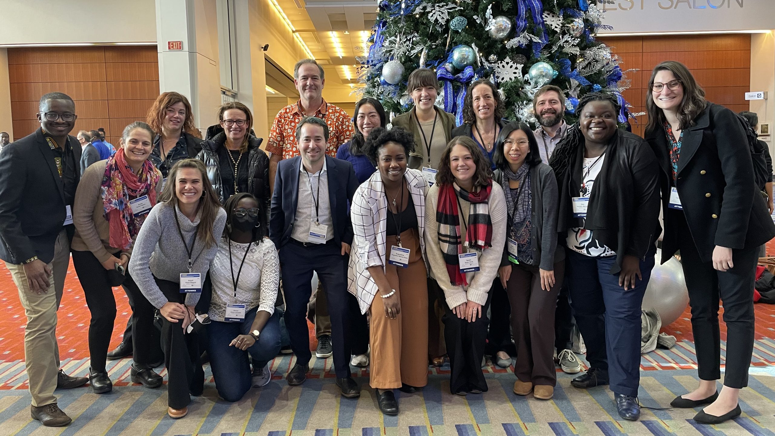 17 UW attendees at D&I 2022 gathered in front of a Christmas tree in the hotel lobby for a group picture.